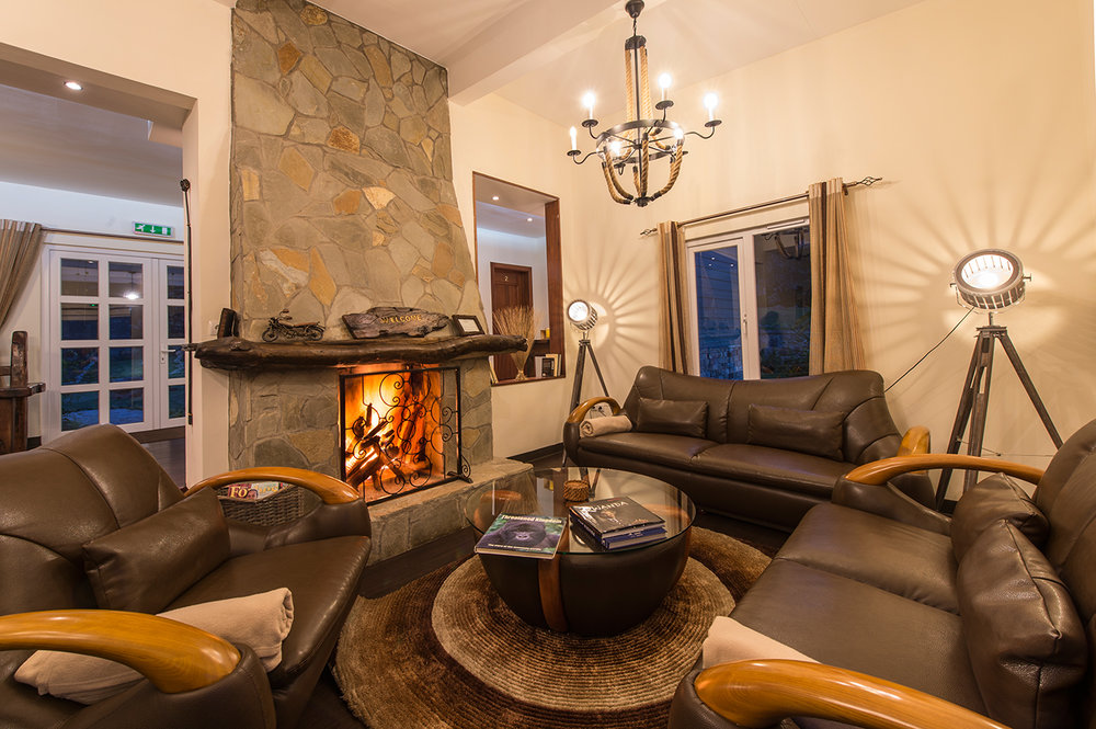 Amakoro Songa Lodge: Sofas mit Kamin Kamin, Lampen, Sofa, Tisch, Amakoro Songa Lodge, Gorilla Tracking, Volcanoes National Park, Afrikarma, Afrikarma Safaris, Afrikarma Safaris. Wildnis. Hautnah., afrikarma.de