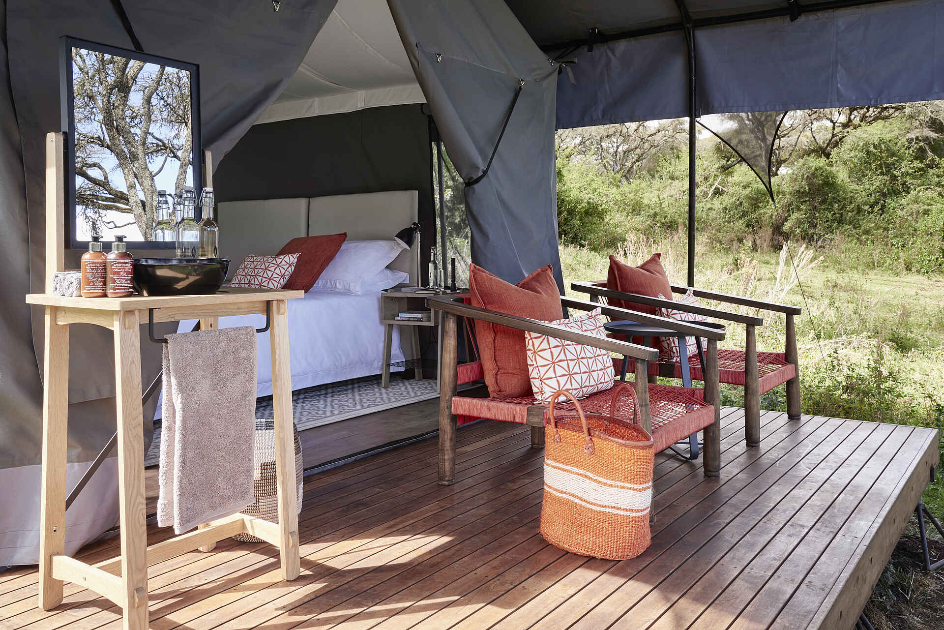 Sanctuary Ngorongoro Crater Camp: Außendeck eines Zeltes Afrikarma, Afrikarma Safaris, Afrikarma Safaris - Wildnis. Hautnah., Afrikarma.de, Sanctuary Ngorongoro Crater Camp, Bäume, Bett, Bücher, Büsche, Decken, Flaschen, Gras, Handtuch, Holzdeck, Kissen, Lampe, Nachttisch, Seifenflaschen, Spiegel, Stühle, Tasche, Taschenlampe, Teppichläufer, Tisch, Wasch-Schüssel, Zelt