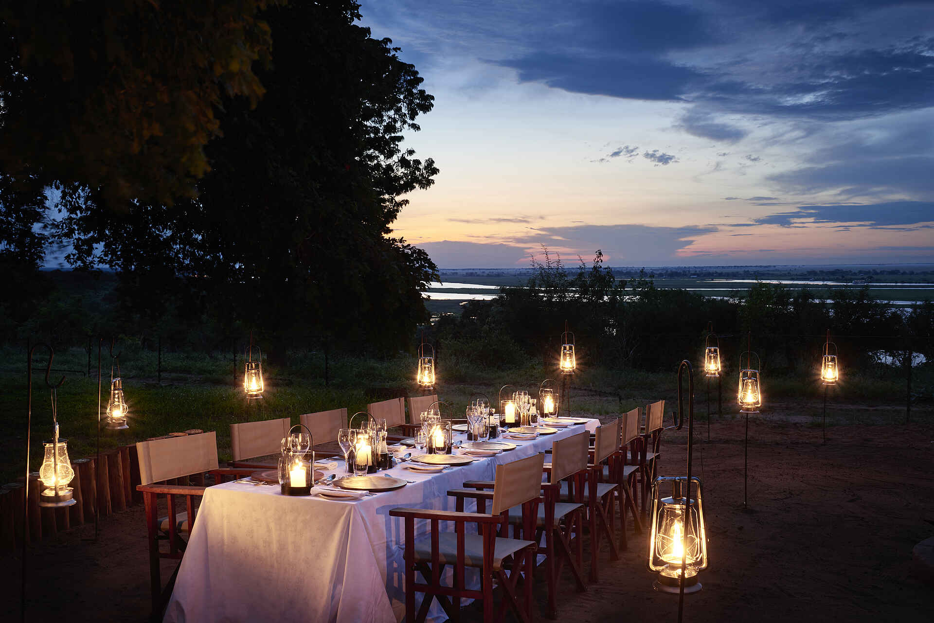 Bäume, Besteck, Büsche, Campingstühle, Fluß, Gedeckter Tisch, Gläser, Gras, Paraffinlampen, Servietten, Teller, Tischdecke, Afrikarma, Afrikarma Safaris, Afrikarma Safaris - Wildnis. Hautnah., Afrikarma.de, Sanctuary Chobe Chilwero