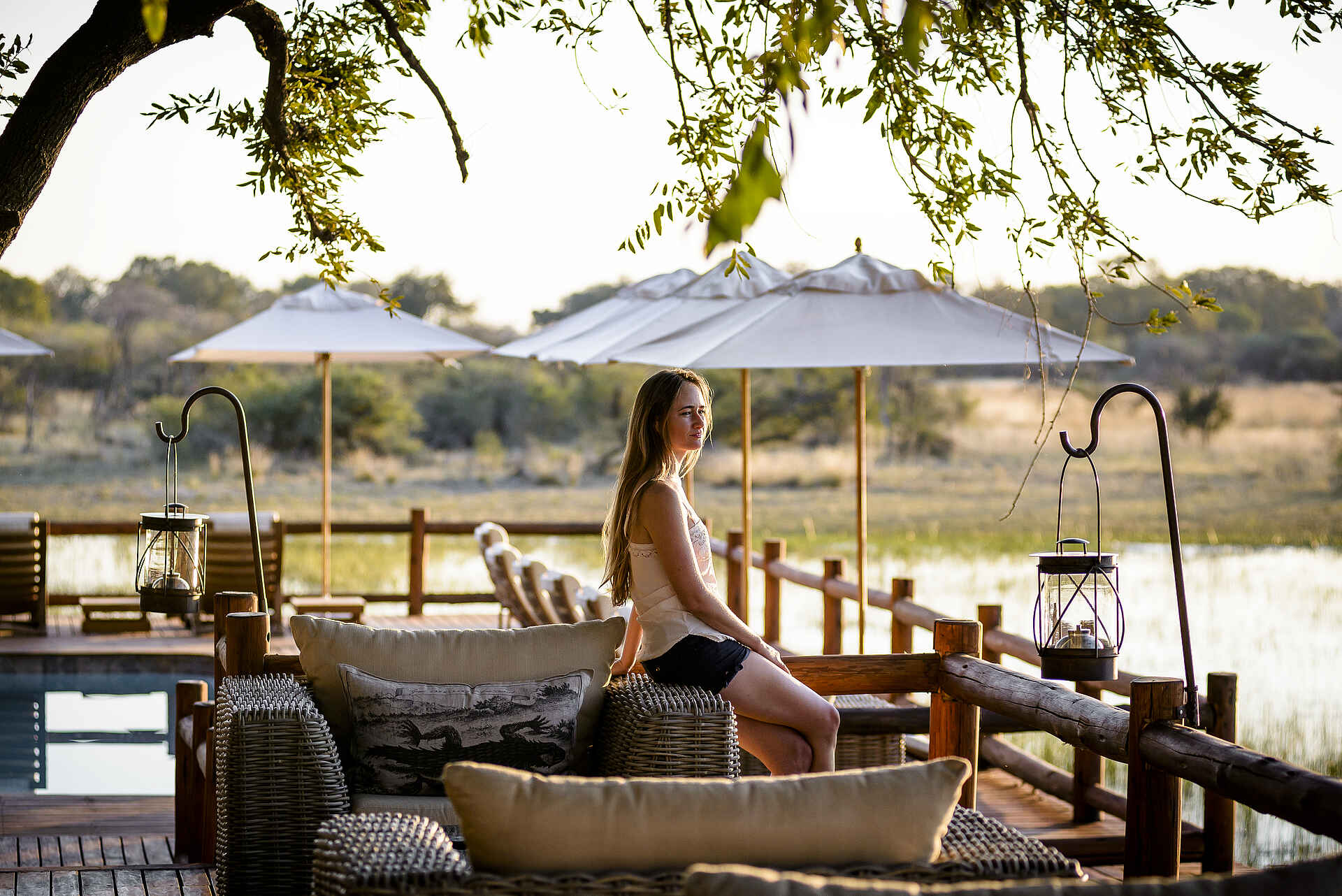 Afrikarma, Afrikarma Safaris, Afrikarma Safaris - Wildnis. Hautnah., Afrikarma.de, Sanctuary Chief's Camp, Bäume, Büsche, Fluß, Gast, Graslandschaft, Holzzaun, Kissen, Paraffinlampen, Sofasitze, Swimmingpool, Liegestühle, Sonnenschirme