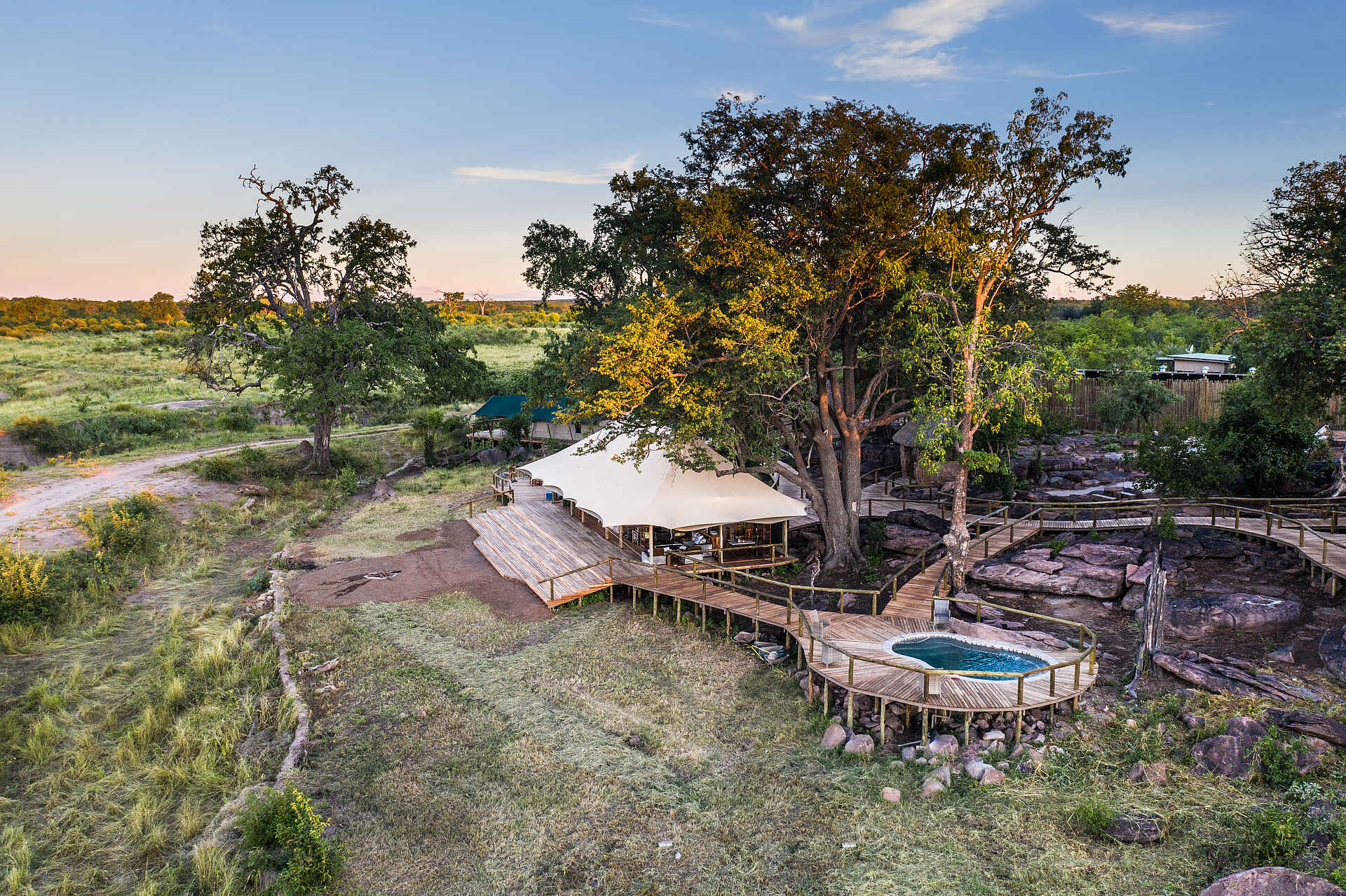 Afrikarma, Afrikarma Safaris, Afrikarma Safaris - Wildnis. Hautnah., Afrikarma.de, Deteema Springs Camp, Bäume, Büsche, Erhöhte Gehwege, Gras, Hauptbereich, Luxuszelte, Swimmingpool