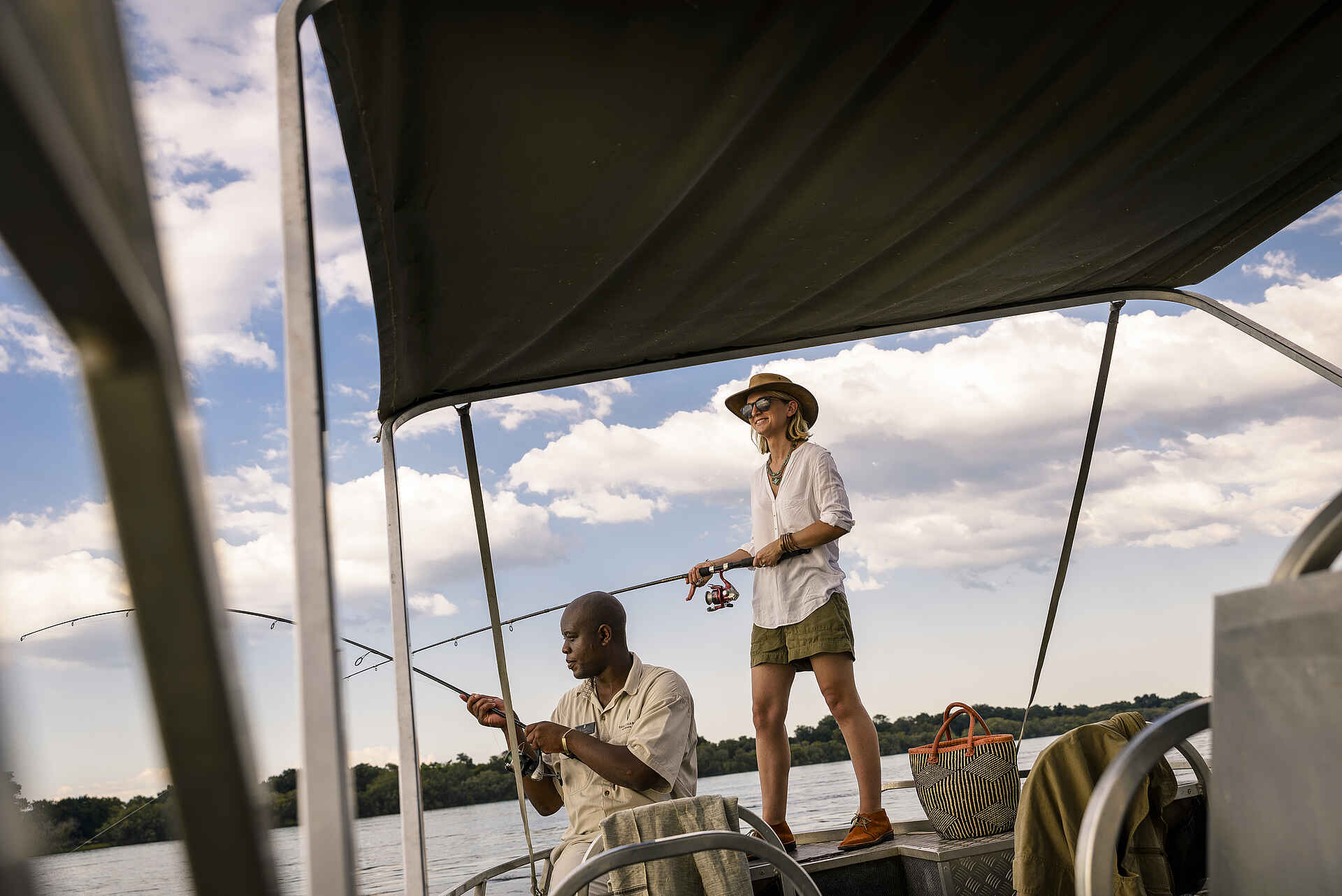 Sanctuary Sussi & Chuma: Fischen auf dem Zambezi River Afrikarma, Afrikarma Safaris, Afrikarma Safaris - Wildnis. Hautnah., Afrikarma.de, Sanctuary Sussi & Chuma, Angelruten, Bäume, Boot, Büsche, Fluß, Gast, Hut, Jacken, Korb, Ranger, Sonnenbrille