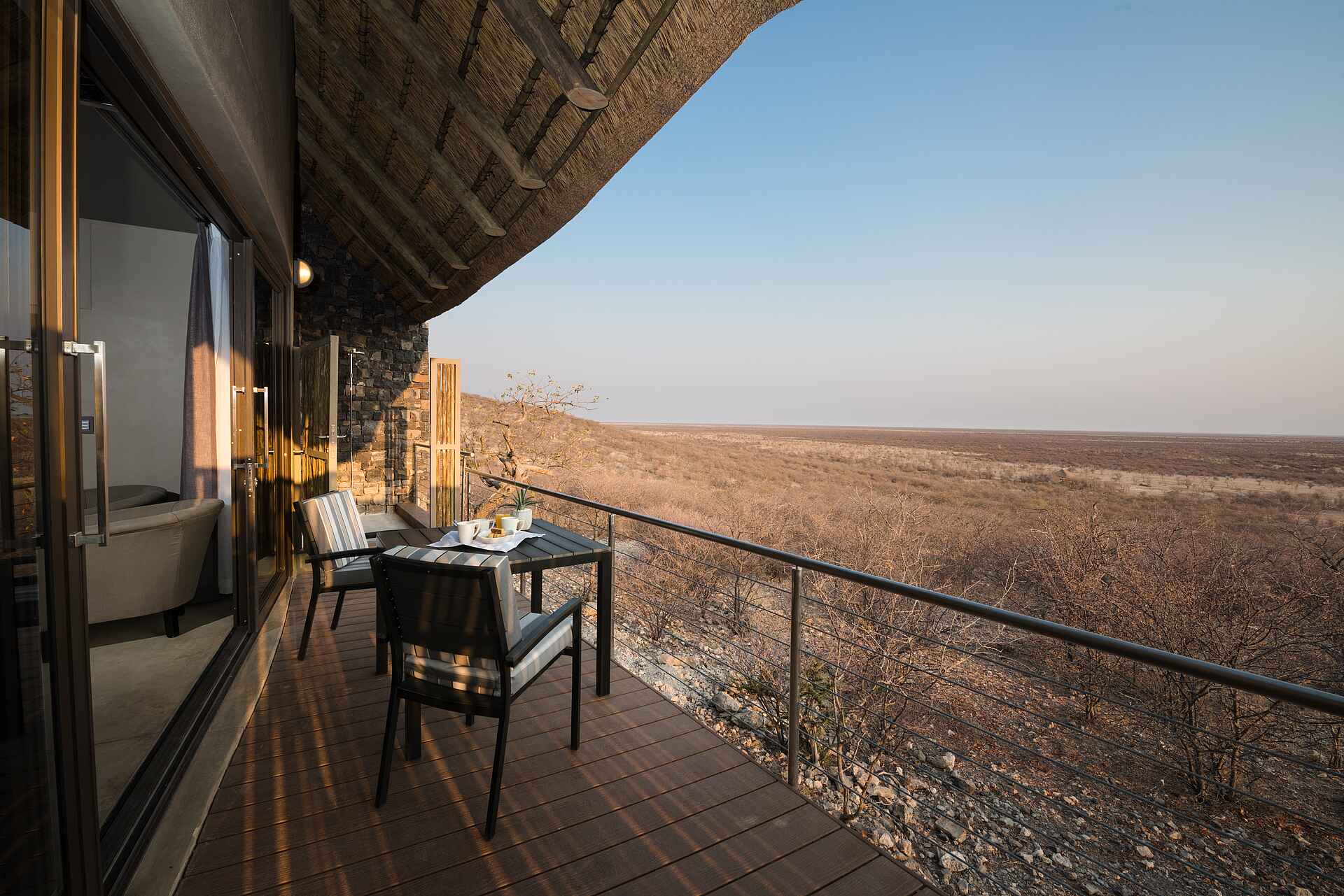 Büsche, Graslandschaft, Holzdeck mit Zaun, Schiebetür, Strohdach, Tisch, Zwei Stühle, Safarihoek Lodge, Afrikarma, Afrikarma Safaris, Afrikarma Safaris - Wildnis. Hautnah., Afrikarma.de