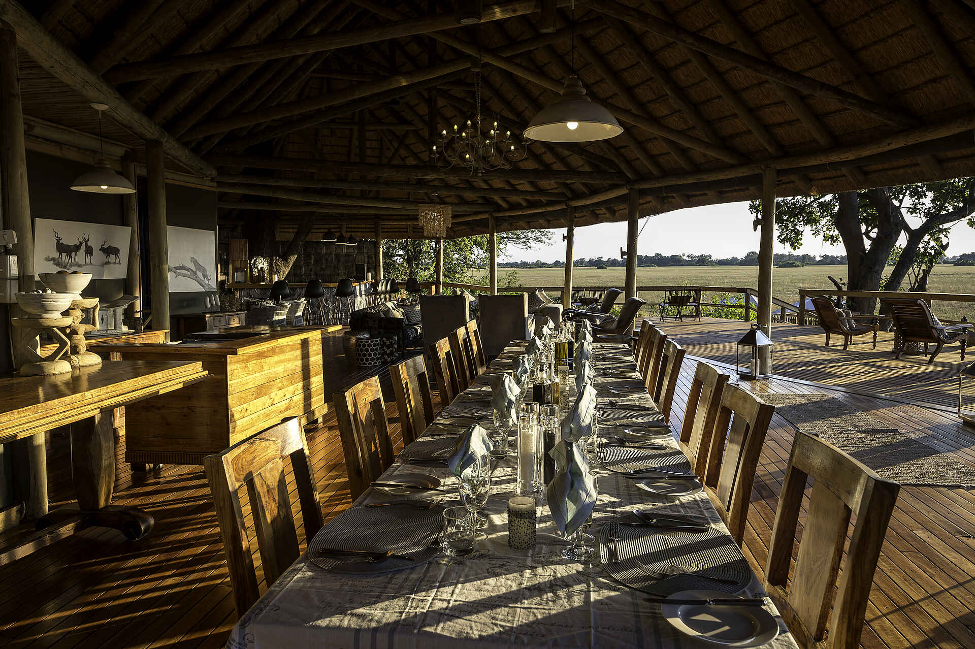 Kwetsani Camp: Esstisch mit Blick auf die Savannenlandschaft Afrikarma, Afrikarma Safaris, Afrikarma Safaris - Wildnis. Hautnah., Afrikarma.de, Kwetsani Camp, Bäume, Besteck, Bilder, Esszimmertisch, Gläser, Holzboden, Holzdeck, Kerzen, Lampen, Liegestühle, Savannenlandschaft, Servietten, Strohdach, Stühle, Teppichläufer, Theke, Tischset