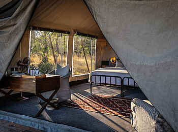 Little Machaba Camp: Interieur eines Gästezelts mit kleinem Holzschreibtisch und Doppelbett