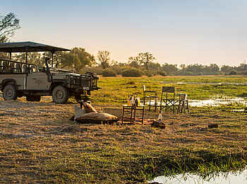 Little Machaba Camp: Eine offenes Safari Fahrzeug mit aufsteigenden Sitzreihen vor kleiner Picknickszenerie