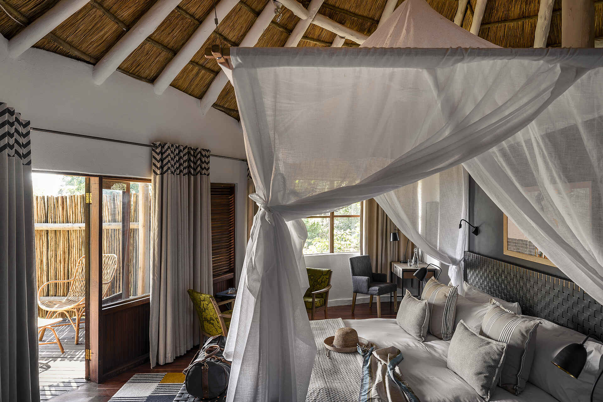 Sanctuary Sussi & Chuma: Schlafzimmer Afrikarma, Afrikarma Safaris, Afrikarma Safaris - Wildnis. Hautnah., Afrikarma.de, Sanctuary Sussi & Chuma, Bäume, Bett, Büsche, Decken, Flasche, Glas, Holzboden, Holzzaun, Hut, Kissen, Lampen, Moskitonetz, Schreibtisch, Stühle, Tasche, Teppichläufer, Tische, Vorhänge