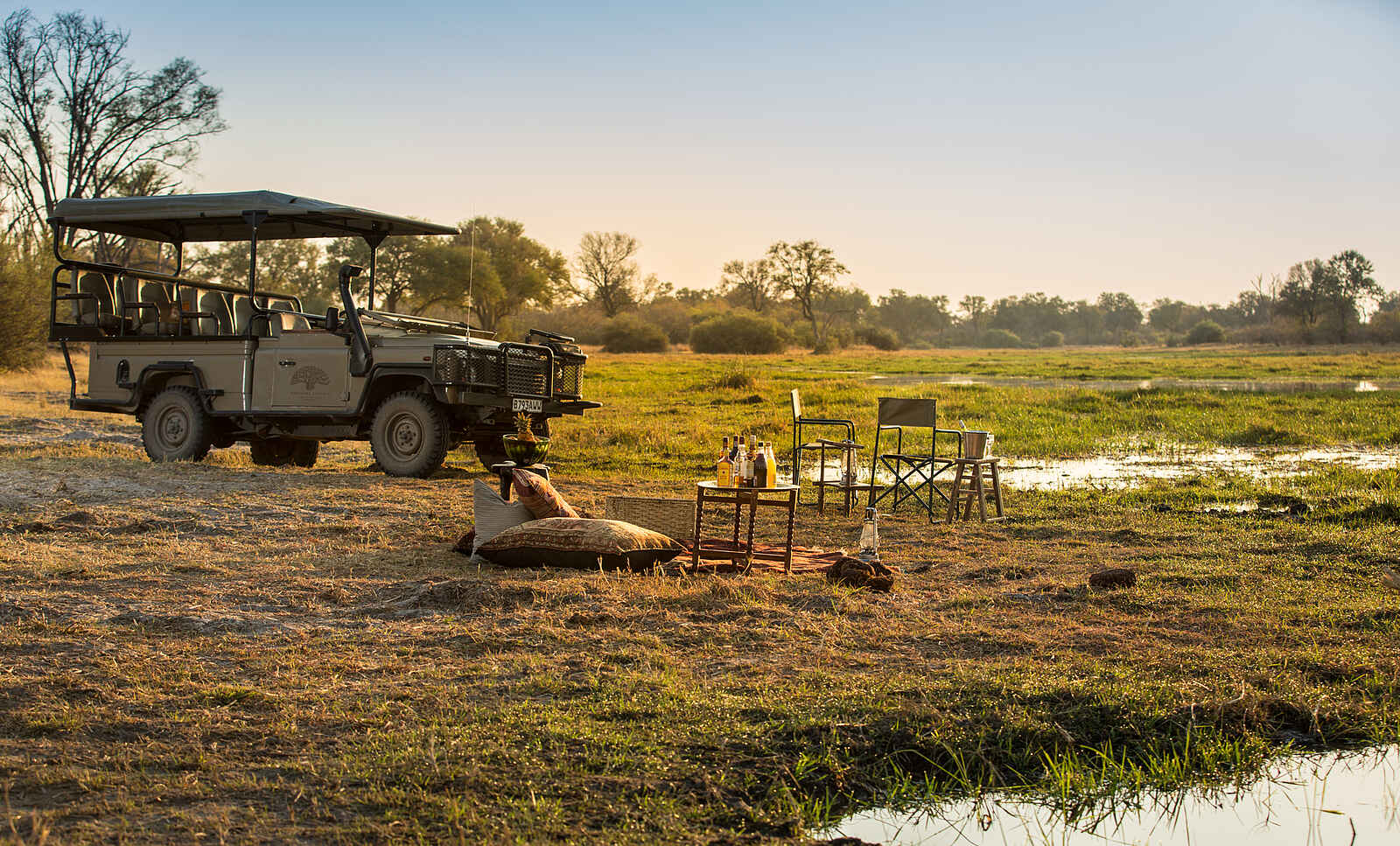 Little Machaba Camp: Eine offenes Safari Fahrzeug mit aufsteigenden Sitzreihen vor kleiner Picknickszenerie Little Machaba Camp: Eine offenes Safari Fahrzeug mit aufsteigenden Sitzreihen vor kleiner Picknickszenerie