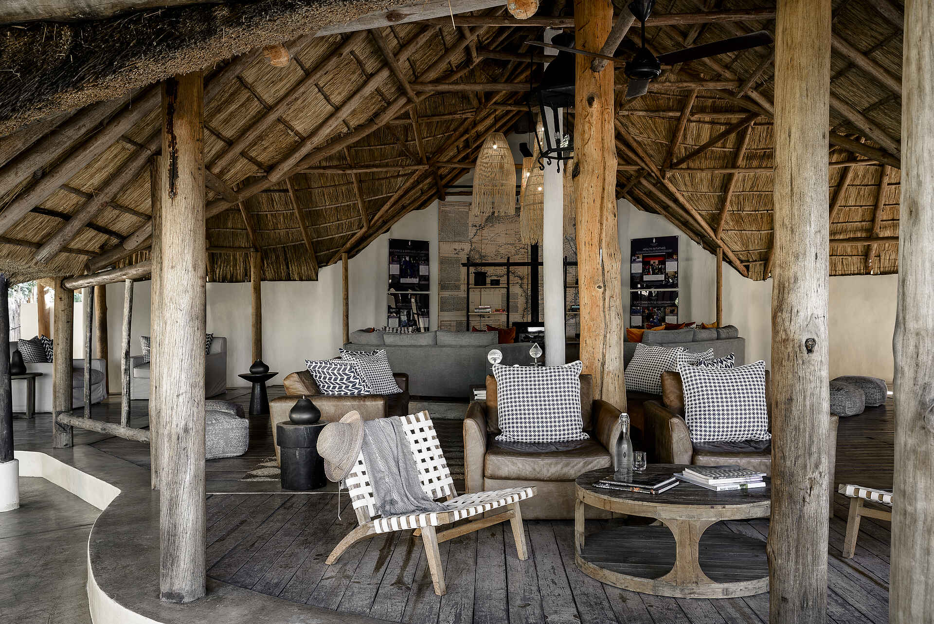 Sanctuary Sussi & Chuma: Explorer-Lounge Afrikarma, Afrikarma Safaris, Afrikarma Safaris - Wildnis. Hautnah., Afrikarma.de, Sanctuary Sussi & Chuma, Bücher, Holzbalken, Hut, Kissen, Lampen, Landkarte, Ornamente, Regale, Sitzkissen, Sofasitze, Strohdach, Tische