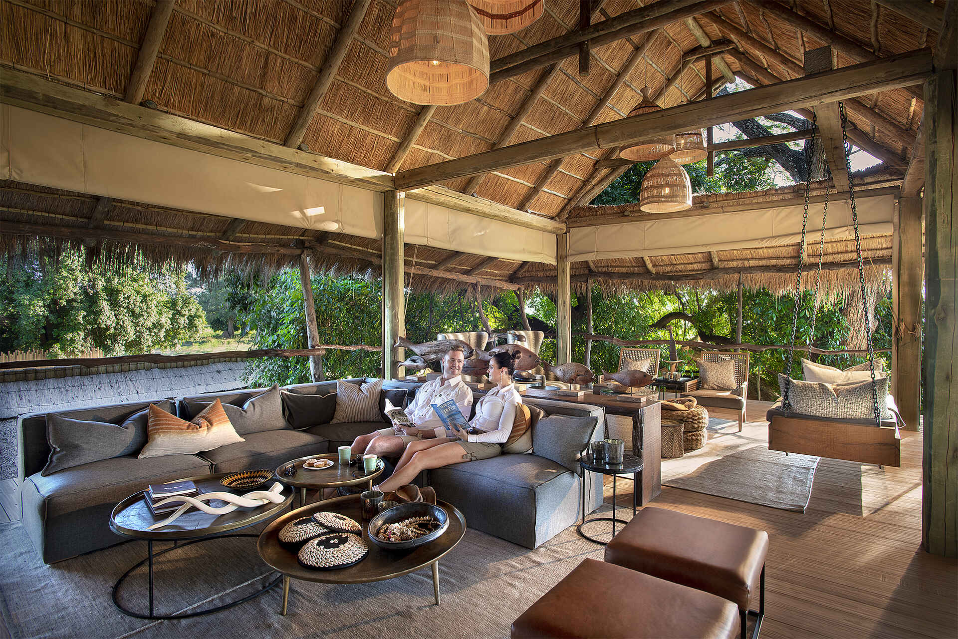 Afrikarma, Afrikarma Safaris, Afrikarma Safaris - Wildnis. Hautnah., Afrikarma.de, Nyamatusi Camp, Bücher, Büsche, Hocker, Holzbalken, Holzboden, Lampen, Ornamente, Schaukel, Sofa, Sofakissen, Strohdach, Stühle, Tassen, Teppiche, Tische, Zwei Gäste