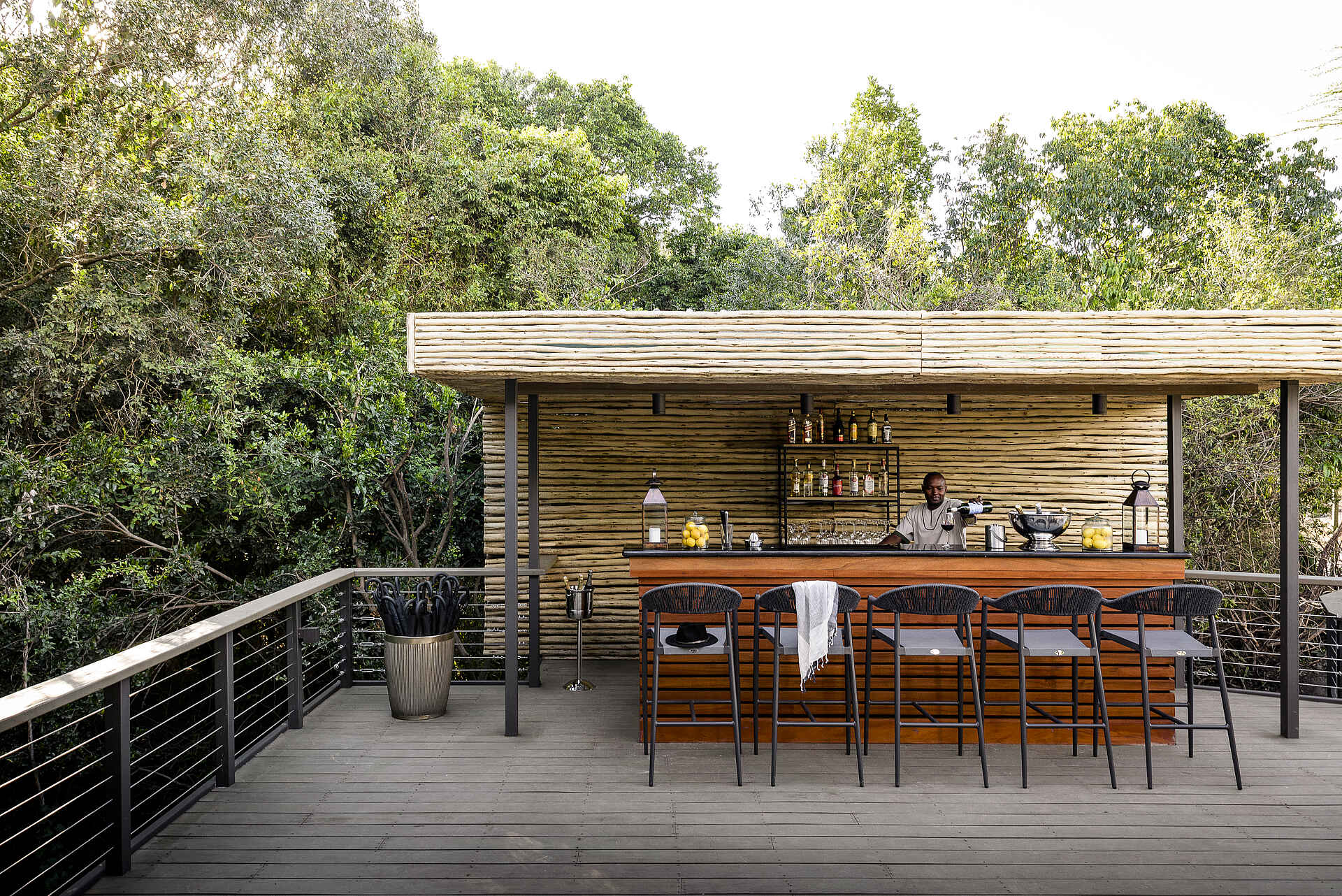 Bar, Barhocker, Barmann, Bäume, Büsche, Flaschen, Früchte, Gläser, Holzdeck, Holzwand, Zaun, Hut, Kerzenlampen, Regenschirme, Weinkühler, Afrikarma, Afrikarma Safaris, Afrikarma Safaris - Wildnis. Hautnah., Afrikarma.de, Sanctuary Olonana