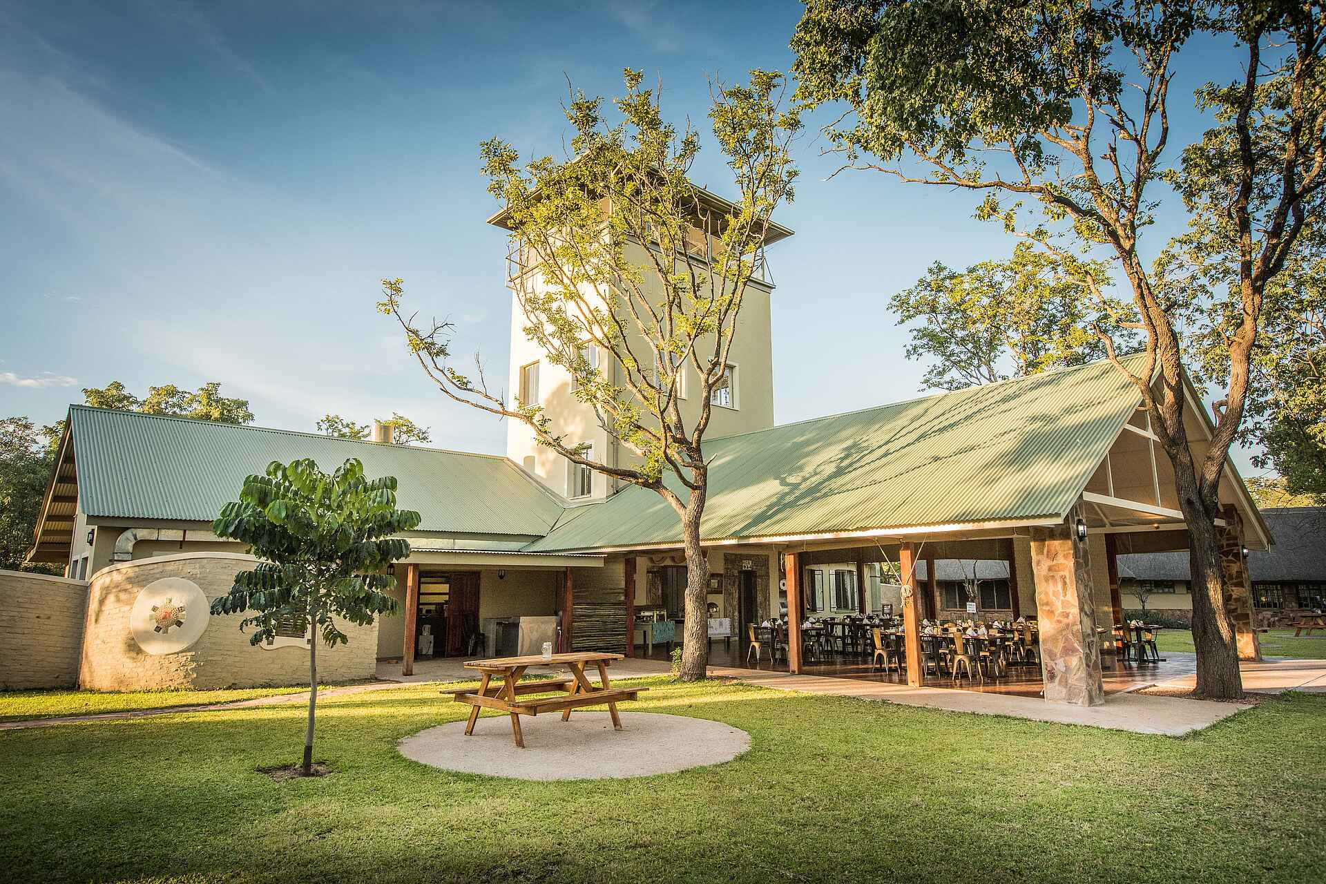 Afrikarma, Afrikarma Safaris, Afrikarma Safaris - Wildnis. Hautnah., Afrikarma.de, Robins Camp, Bäume, Gras, Holzbank, Stühle, Tische