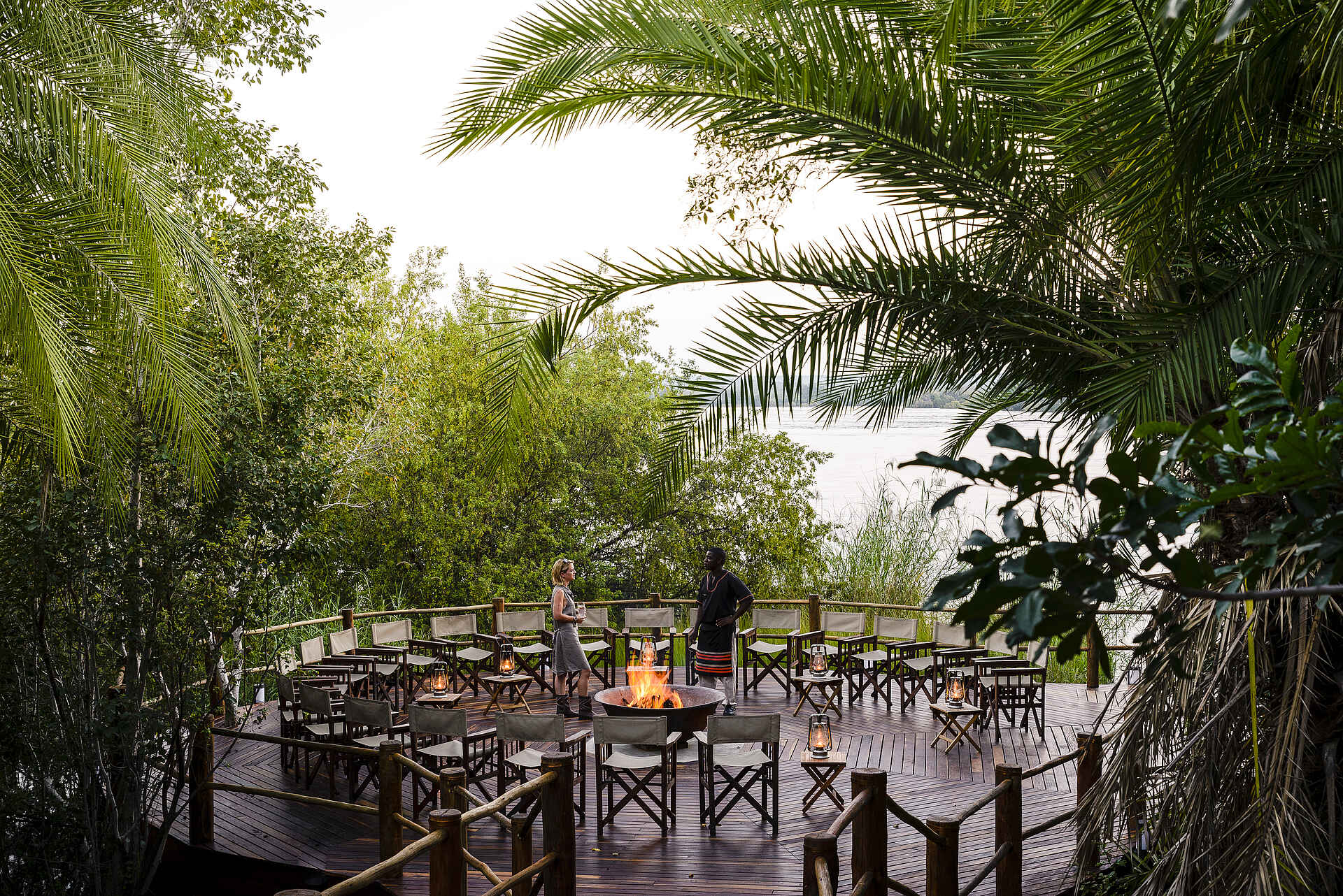 Sanctuary Sussi & Chuma: Boma Afrikarma, Afrikarma Safaris, Afrikarma Safaris - Wildnis. Hautnah., Afrikarma.de, Sanctuary Sussi & Chuma, Angestellter, Bäume, Boma, Büsche, Campingstühle, Campingtische, Fluß, Gast, Glas, Holzboden, Holzzaun, Lagerfeuer, Paraffinlampen