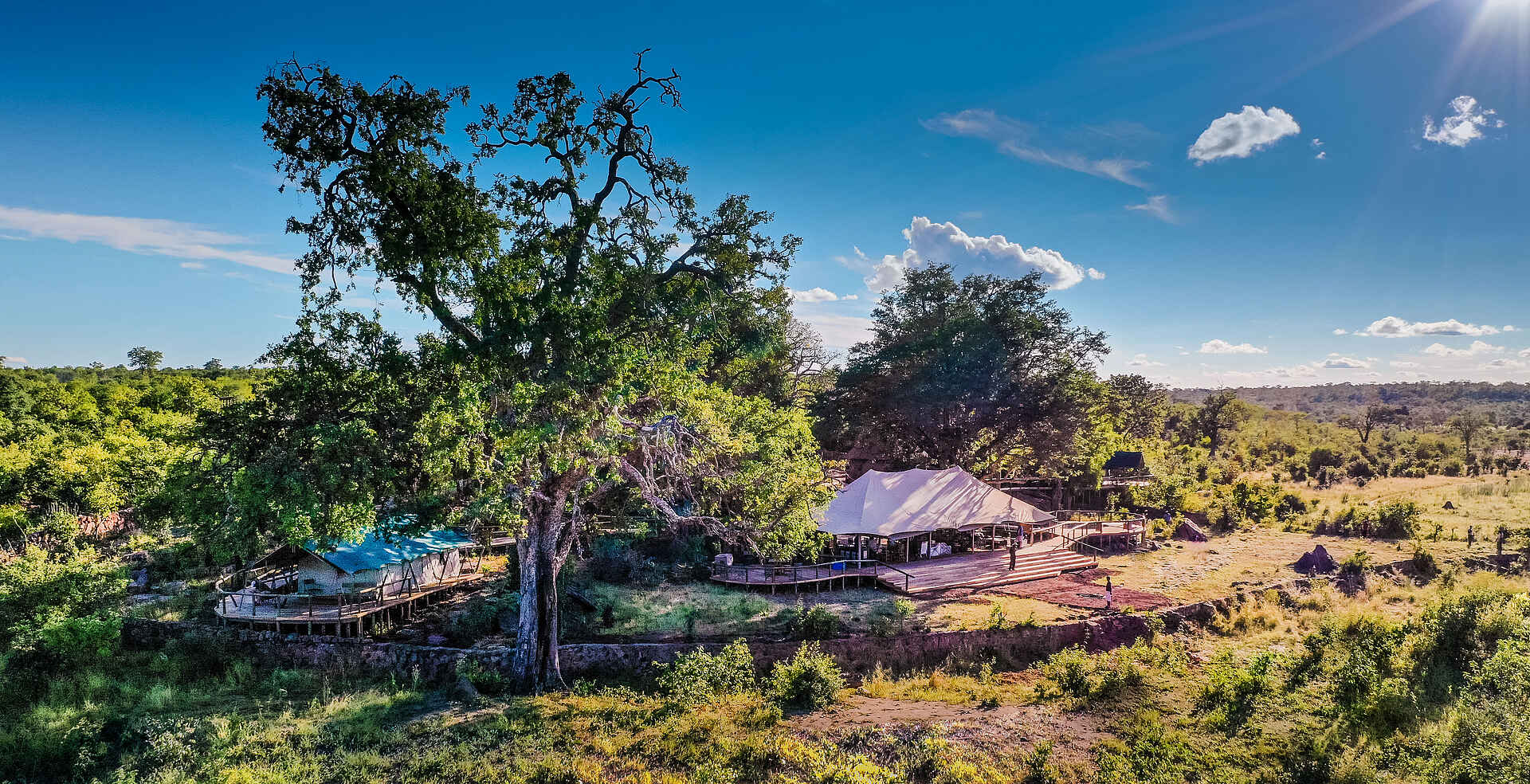 Afrikarma, Afrikarma Safaris, Afrikarma Safaris - Wildnis. Hautnah., Afrikarma.de, Deteema Springs Camp, Bäume, Büsche, Eröhte Gehwege, Gras, Hauptbereich, Luxuszelte, Steinmauer