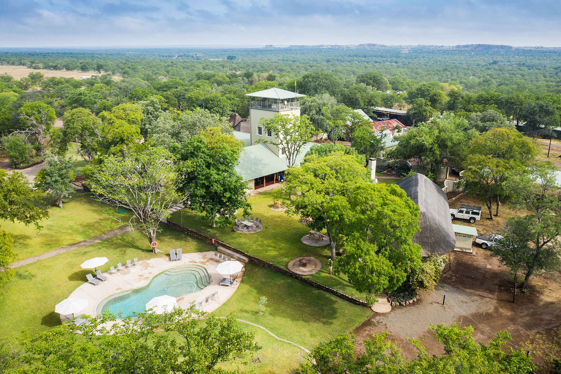 Afrikarma, Afrikarma Safaris, Afrikarma Safaris - Wildnis. Hautnah., Afrikarma.de, Robins Camp, Autos, Luftaufnahme, Bäume, Büsche, Chalets, Gras, Liegestühle, Sonnenschirme, Strohdach, Swimmingpool, Bänke, Stühle, Tische