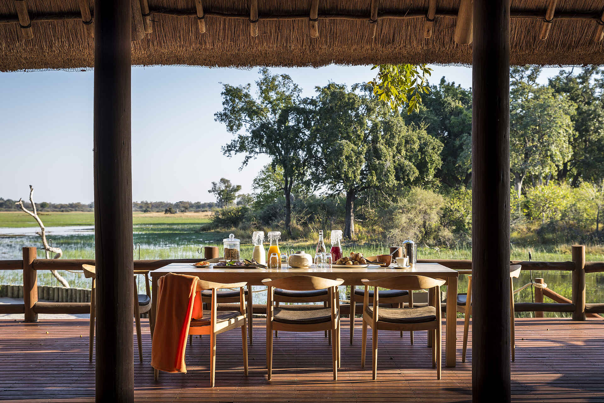 Afrikarma, Afrikarma Safaris, Afrikarma Safaris - Wildnis. Hautnah., Afrikarma.de, Sanctuary Chief's Camp, Bäume, Brot, Büsche, Früchte, Handtuch, Holzdeck, Holzzaun, Säfte, Strohdach, Stühle, Tisch, Gläser, Tassen, Teller, Fluß