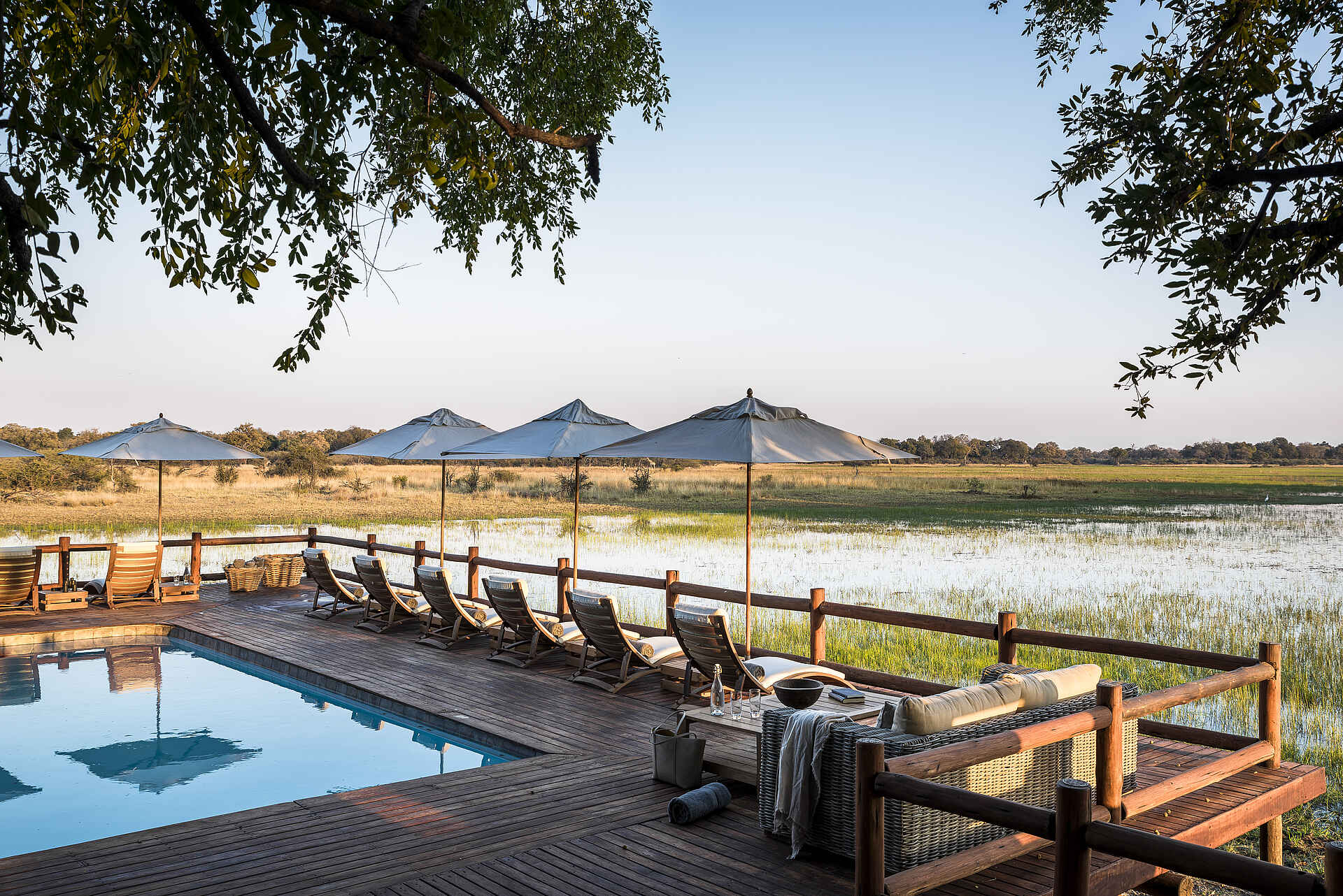 Afrikarma, Afrikarma Safaris, Afrikarma Safaris - Wildnis. Hautnah., Afrikarma.de, Sanctuary Chief's Camp, Bäume, Bücher, Büsche, Fluß, Handtücher, Holzdeck, Körbe, Liegestühle, Ornamente, Savannenlandschaft, Sonnenschirme, Swimmingpool