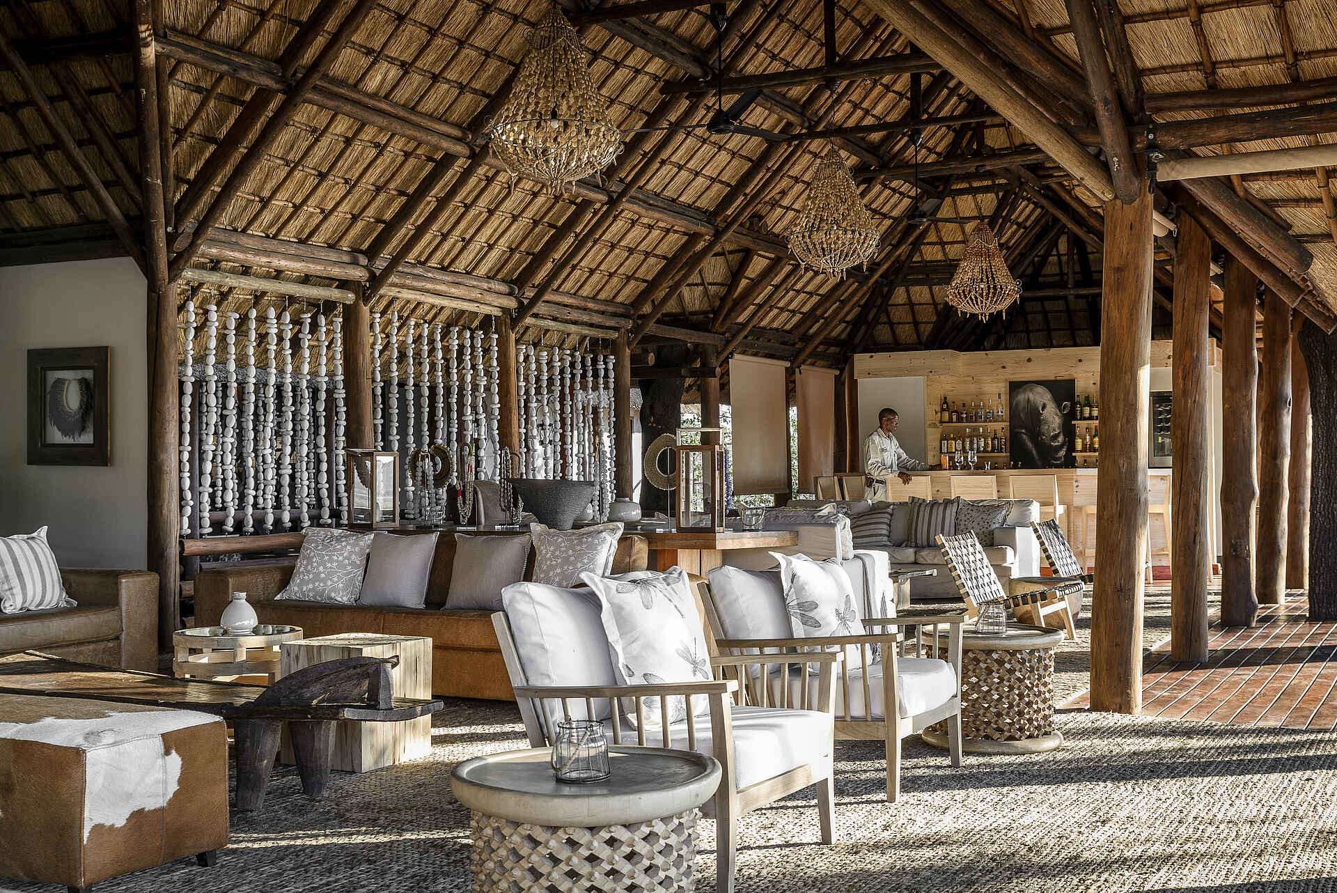 Afrikarma, Afrikarma Safaris, Afrikarma Safaris - Wildnis. Hautnah., Afrikarma.de, Sanctuary Chief's Camp, Angestellter, Bartheke, Bilder, Flaschen, Holzbalken, Lampen, Ornamente, Sofasitze, Strohdach, Tische, Kissen